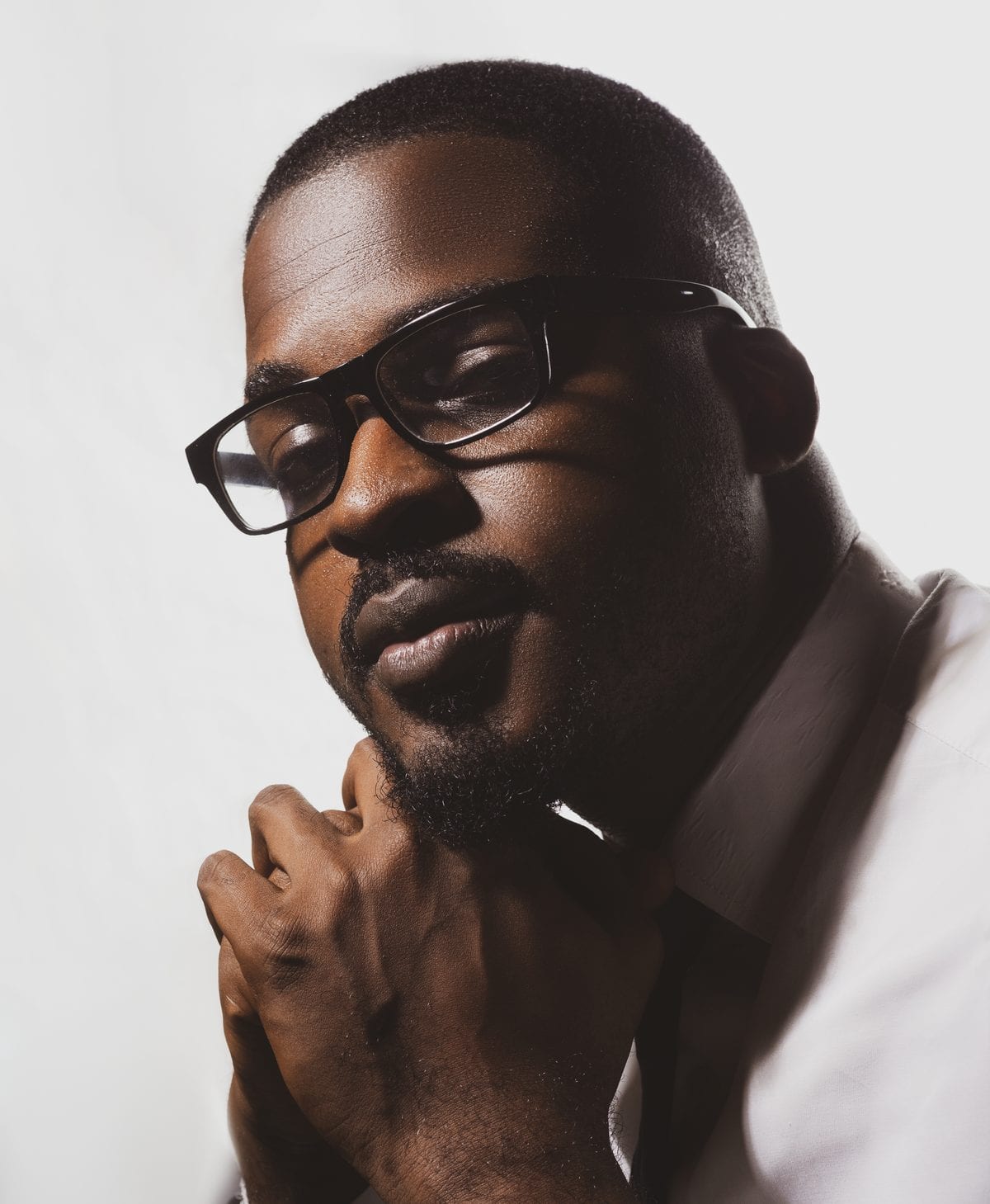 Tolu Afilaka in glasses, hand resting against his chin, looking down in thought.